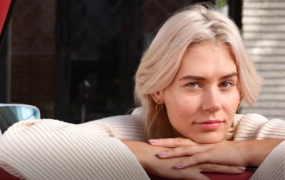 Patient looks into the camera with slight, knowing smile, with chin resting on folded hands.